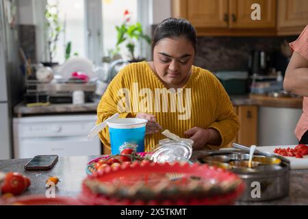 Jeune femme trisomique préparant la nourriture en cuisine Banque D'Images