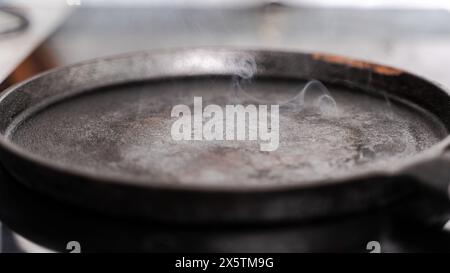 Une poêle en fonte fume sur le poêle. Une poêle prête à cuire. foyer sélectionné. Photo de haute qualité Banque D'Images