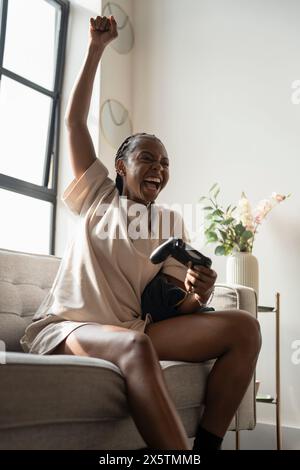 Jeune femme excitée jouant à des jeux vidéo tout en étant assise sur un canapé à la maison Banque D'Images