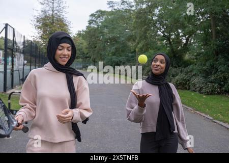 Deux femmes en hijabs marchant dans le parc avec raquette de tennis et balle Banque D'Images