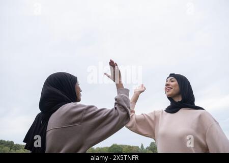 Deux femmes souriantes en hijabs donnant haut cinq à l'extérieur Banque D'Images