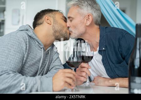 Couple masculin buvant du vin rouge et s'embrassant à la maison Banque D'Images