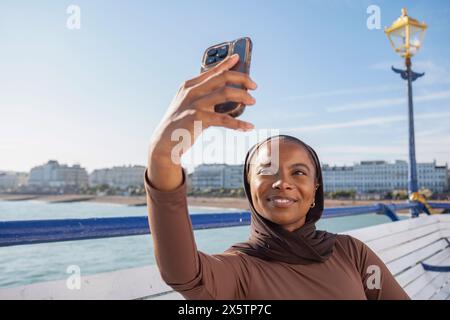 Femme musulmane prenant selfie avec vue sur la mer le jour ensoleillé Banque D'Images