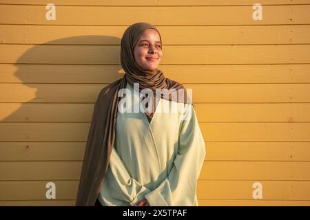 Portrait d'une jeune femme musulmane regardant loin contre le mur jaune Banque D'Images