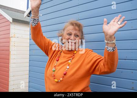 Portrait d'une femme âgée souriante avec les mains levées contre la hutte bleue Banque D'Images