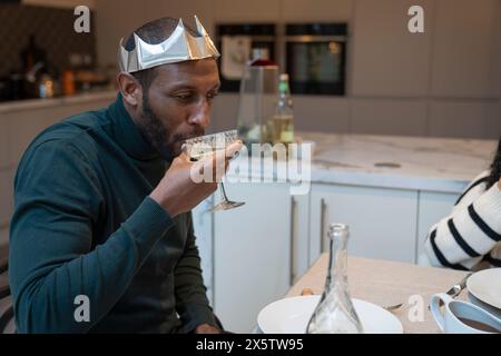 Homme portant une couronne de papier buvant du vin à la table du dîner de Noël Banque D'Images