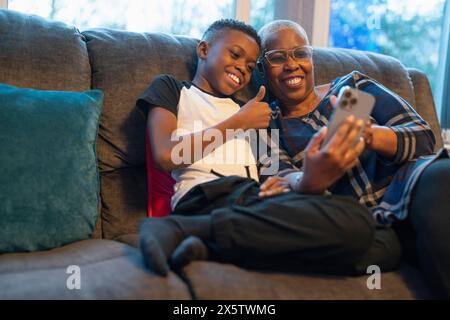 Grand-mère et petit-fils avec téléphone intelligent assis sur le canapé Banque D'Images