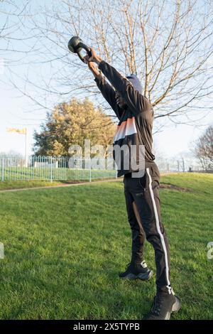 Homme athlétique faisant exercice d'oscillation kettlebell dans le parc Banque D'Images
