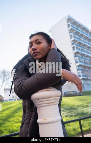 Portrait d'une femme en pardessus appuyée sur un poteau Banque D'Images