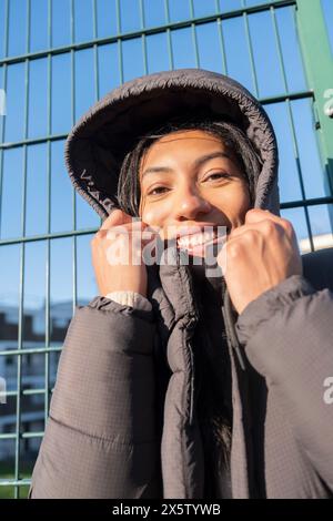 Portrait de femme souriante en pardessus avec capuche debout à la clôture Banque D'Images