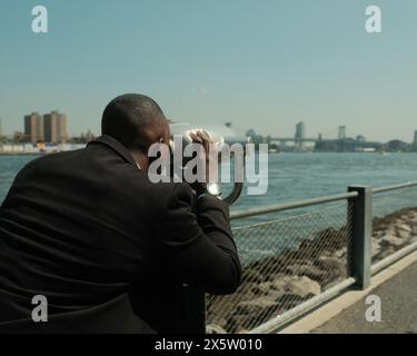 USA, New York City, homme en costume regardant la ville à travers des jumelles à pièces Banque D'Images