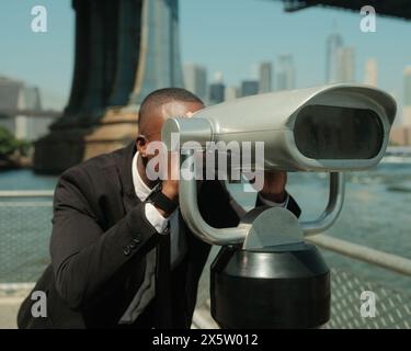 USA, New York City, homme en costume regardant la ville à travers des jumelles à pièces Banque D'Images