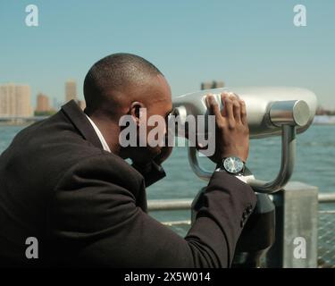 USA, New York City, homme en costume regardant la ville à travers des jumelles à pièces Banque D'Images