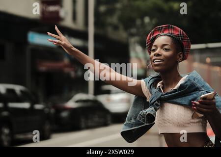 USA, New York, femme élégante souriante hélant taxi dans la rue Banque D'Images