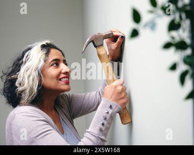 Femme martelant un clou dans le mur de la maison Banque D'Images