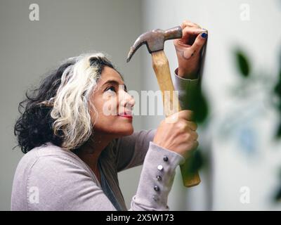 Femme martelant un clou dans le mur de la maison Banque D'Images