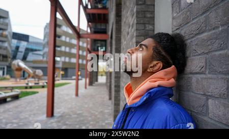 Jeune homme portant un blouson bleu appuyé sur le mur Banque D'Images