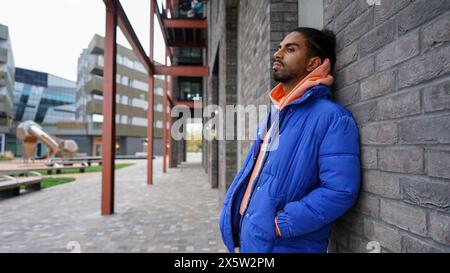 Jeune homme portant un blouson bleu appuyé sur le mur Banque D'Images