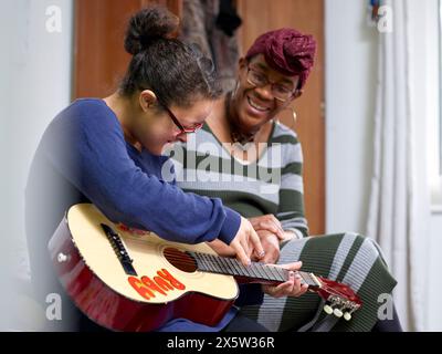 Mère aidant sa fille avec le syndrome de Down jouant de la guitare dans la chambre Banque D'Images