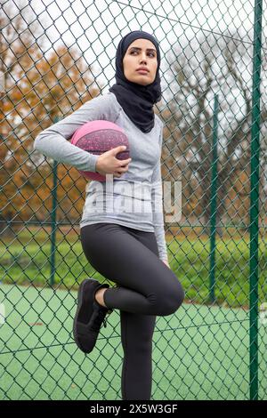 Femme en hijab avec ballon de basket-ball appuyé sur la clôture Banque D'Images