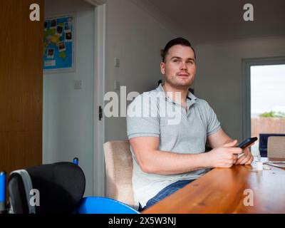 Homme assis à table avec téléphone intelligent et test de coronavirus à domicile Banque D'Images