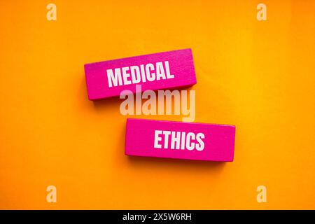 Mots d'éthique médicale écrits sur des blocs de bois roses avec fond orange. Symbole conceptuel de l'éthique médicale. Copier l'espace. Banque D'Images
