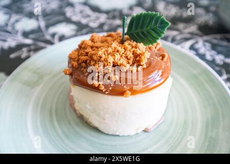 Détail d'une table de bonbons. Vue de face. Un petit cheesecake rond sur une assiette sur une belle nappe à décoration florale Banque D'Images