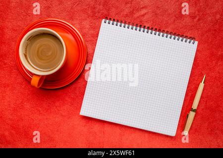 cahier à spirale vierge avec papier ligné, posé à plat avec café sur papier d'art texturé rouge Banque D'Images