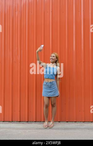 Plein corps de belle fille asiatique avec des cheveux blonds sur fond orange à l'extérieur Banque D'Images