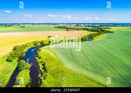 Une rivière serpente à travers une campagne verdoyante en Suède, entourée de champs verdoyants et d'une végétation vibrante sous un ciel bleu clair. Banque D'Images