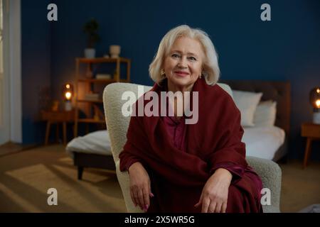 Portrait de belle femme senior bien entretenue assise sur un fauteuil à la maison Banque D'Images