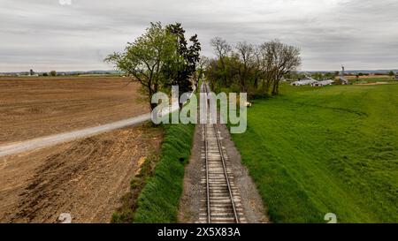 Un train descend une voie à côté d'un champ. Le train est noir et de la vapeur sort de l'avant Banque D'Images