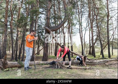 Trois touristes ramassent du bois de chauffage pour un feu dans une forêt de pins. Banque D'Images