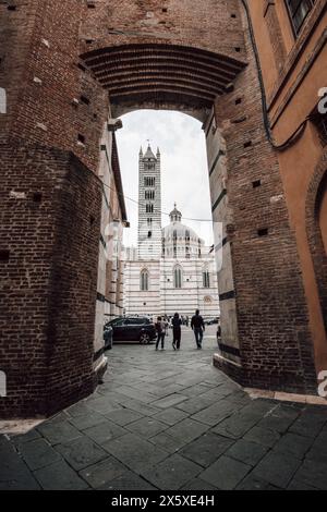 Le Duomo di Siena - Cathédrale de Sienne - en Toscane, Italie, avec des gens marchant sous une grande arche sous le Panorama dal Facciatone par un jour nuageux. Banque D'Images