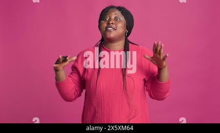 Femelle afro-américaine en pull rose avec les mains couvrant son visage exprimant la colère et la gêne. Jeune femme influenceuse de mode ne criant pas tout en regardant la caméra. Banque D'Images