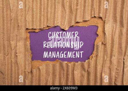 Mots de gestion de la relation client écrits sur du papier cartonné déchiré avec fond violet. Symbo CRM conceptuel de gestion de la relation client Banque D'Images