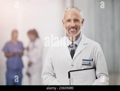 Médecin senior, homme et portrait avec checklist, sourire et fierté pour la carrière dans le couloir à l'hôpital. Médecin mature, personne et presse-papiers pour info, notes Banque D'Images