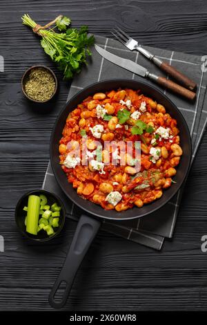 gigantes plaki, haricots géants grecs cuits au four dans une sauce tomate épaisse saupoudrée de fromage feta et de coriandre fraîche sur poêle sur une table en bois noir avec r Banque D'Images