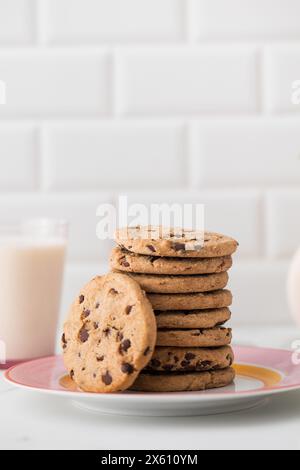 Les biscuits sont étalés sur une assiette, un verre de lait frais. Biscuits faits maison avec pépites de chocolat. Banque D'Images