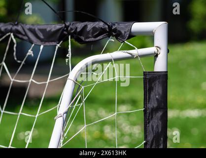 Gros plan d'un but de football de bricolage fait de tuyaux en PVC blanc avec un filet usé dans un cadre de parc, parfait pour les thèmes sportifs récréatifs ou communautaires. Banque D'Images