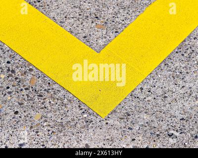 Vue rapprochée de la ligne jaune en forme de V sur un revêtement en béton texturé, couleurs contrastées et détails géométriques. Banque D'Images