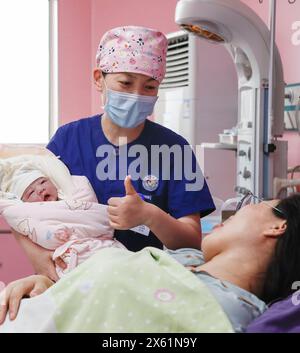 Pékin, province chinoise du Jiangsu. 12 mai 2024. Une infirmière tient un nouveau-né et interagit avec la mère dans un hôpital de la ville de Xuzhou, dans la province du Jiangsu de l'est de la Chine, le 12 mai 2024. Dimanche marquait la 113e Journée internationale des infirmières. Crédit : Bai Xue/Xinhua/Alamy Live News Banque D'Images