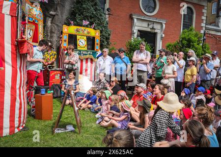 Londres, Royaume-Uni. 12 mai 2024. Enfants et adultes regardent un spectacle de l'un des membres de la Punch & Judy Fellowship. L'après-midi, un certain nombre de spectacles traditionnels et modernes de Punch et Judy divertissent la foule. Les marionnettistes de tout le pays se rassemblent pour le festival annuel de mai Fayre and Puppet. Il se déroule dans les jardins de l'église St Paul (également appelée église de l'acteur), Covent Garden et comprend un service religieux, une procession, des spectacles de Punch et Judy, des ateliers, des stands et des divertissements en famille. Crédit : Imageplotter/Alamy Live News Banque D'Images