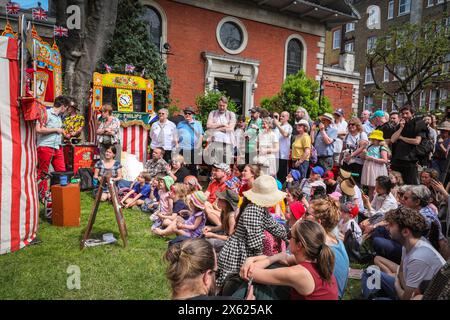 Londres, Royaume-Uni. 12 mai 2024. Enfants et adultes regardent un spectacle de l'un des membres de la Punch & Judy Fellowship. L'après-midi, un certain nombre de spectacles traditionnels et modernes de Punch et Judy divertissent la foule. Les marionnettistes de tout le pays se rassemblent pour le festival annuel de mai Fayre and Puppet. Il se déroule dans les jardins de l'église St Paul (également appelée église de l'acteur), Covent Garden et comprend un service religieux, une procession, des spectacles de Punch et Judy, des ateliers, des stands et des divertissements en famille. Crédit : Imageplotter/Alamy Live News Banque D'Images