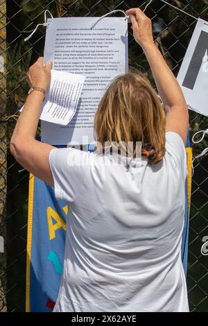 Lakenheath, Royaume-Uni. 11 mai 2024. Sue Wright de Norwich CND fixe un avis sur la clôture de périmètre de la RAF Lakenheath déclarant qu'elle est une zone exempte d'armes nucléaires lors d'une manifestation de la campagne pour le désarmement nucléaire (CND) devant la base. Les manifestants ont appelé le gouvernement britannique à refuser la livraison de bombes nucléaires américaines B61-12 à la base. Il faisait partie d'une journée nationale d'action de la CND. Crédit : Mark Kerrison/Alamy Live News Banque D'Images