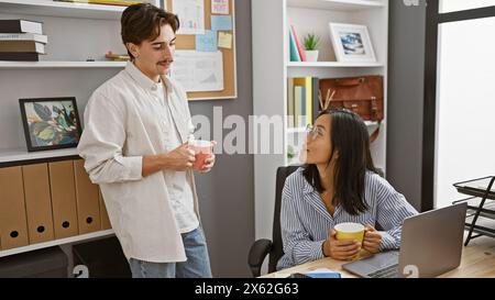 Un homme et une femme, collègues, s'engagent dans une conversation détendue autour d'un café dans un bureau moderne. Banque D'Images