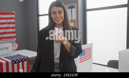 Une jeune femme hispanique avec un autocollant «j'ai voté» se pointe vers elle dans une salle d'un collège électoral américain avec des drapeaux. Banque D'Images