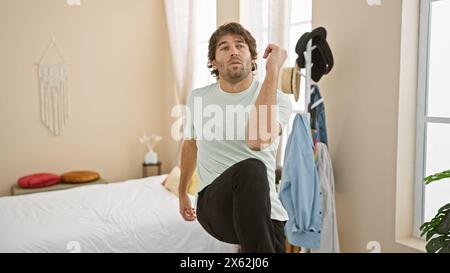 Un jeune homme barbu en tenue décontractée s'étire dans une chambre aux tons neutres. Banque D'Images