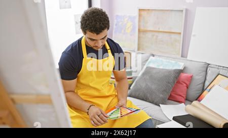 Un homme réfléchi dans un tablier jaune examine les échantillons de couleurs au studio d'art. Banque D'Images