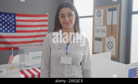 Jeune femme hispanique dans des lunettes au bureau de vote américain avec nous drapeaux et autocollant «j'ai voté» Banque D'Images